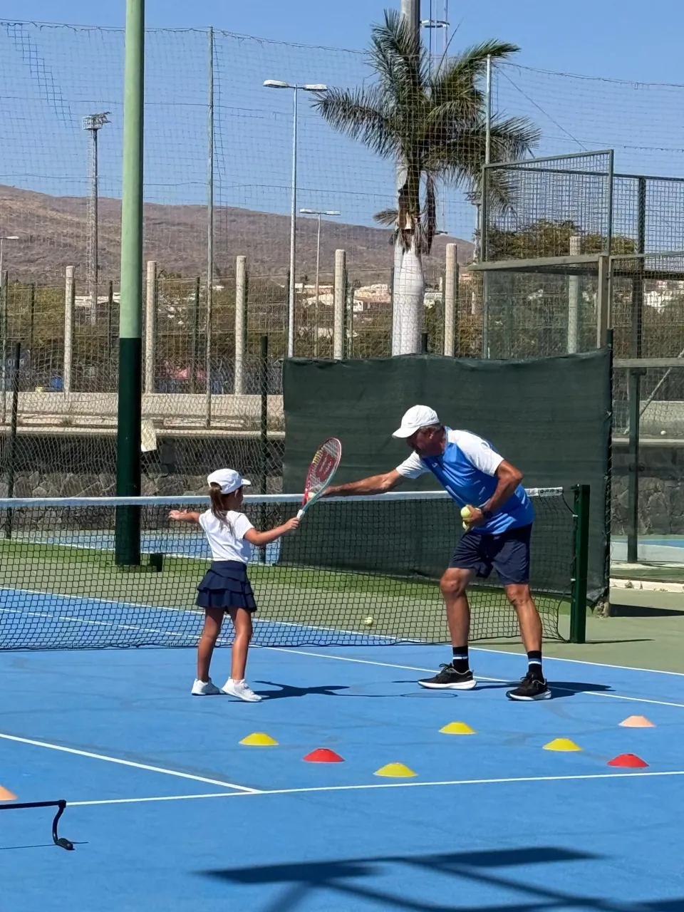 Juan enseñando una volea a una niña junto a la red
